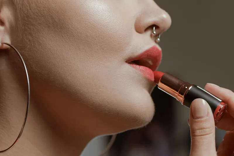 Close-up of a woman with deep skin applying a rich rosy brown lipstick