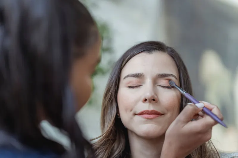 Makeup artist applying eyeshadow to a client's closed eyelid with a small brush