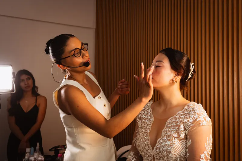 A makeup artist with a headset mic applies makeup to a bride before her wedding