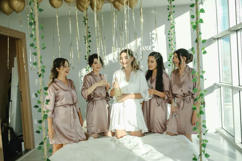 A bride and her bridesmaids in robes celebrate together in a bright room before the wedding