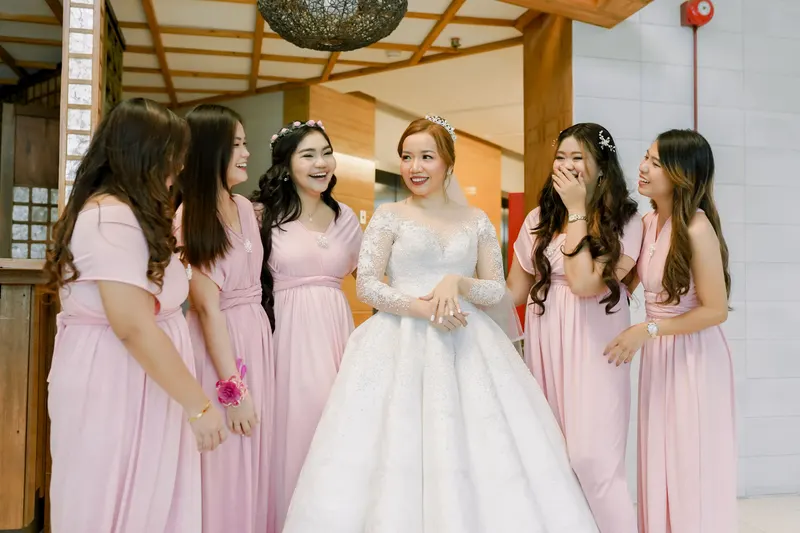 Bride in a lace gown laughing with bridesmaids in pink dresses with long and shoulder-length hair