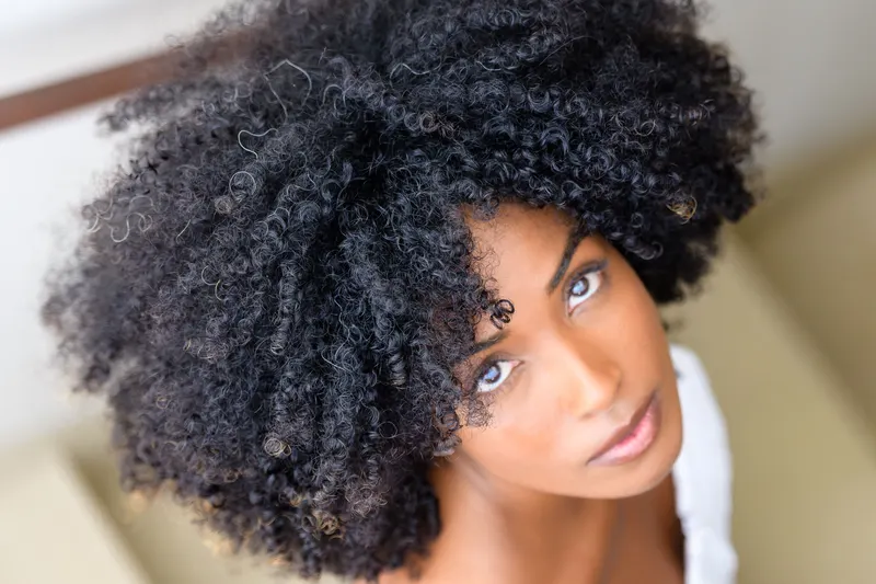 Woman with full, natural coily hair looking up at the camera