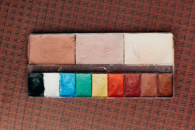 Cream makeup palette with skin-tone shades above green, yellow, orange and red corrector colors