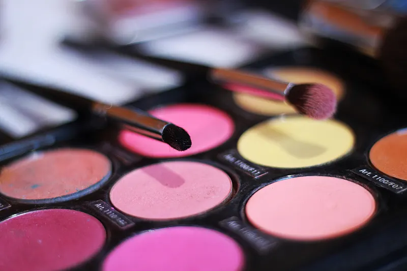 A brush resting on a palette of rosy pink and berry blushes.