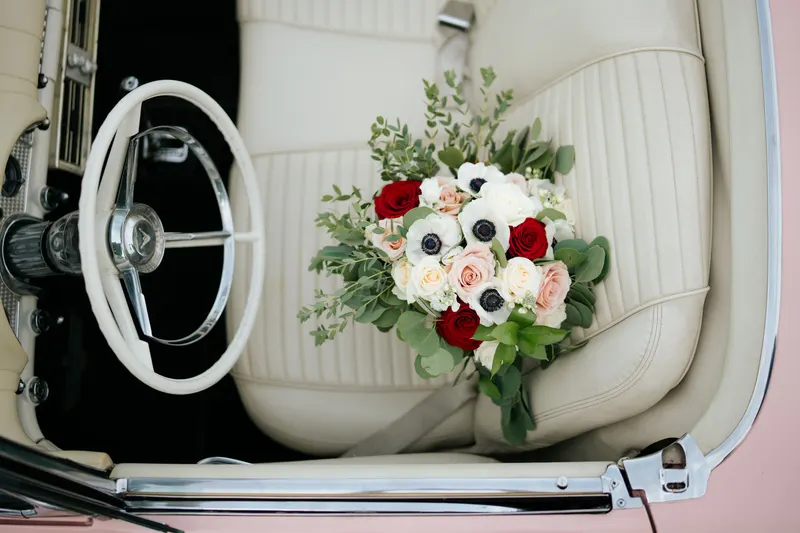 A bouquet of red roses, white roses and white anemones on the crisp white seat of a vintage car, the clear red and white contrast of a cool winter color palette.