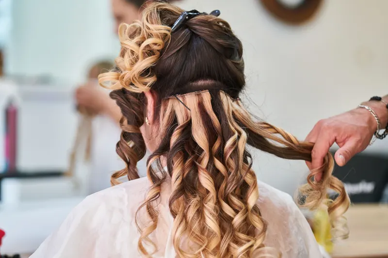 A stylist curls long hair in sections with a curling iron