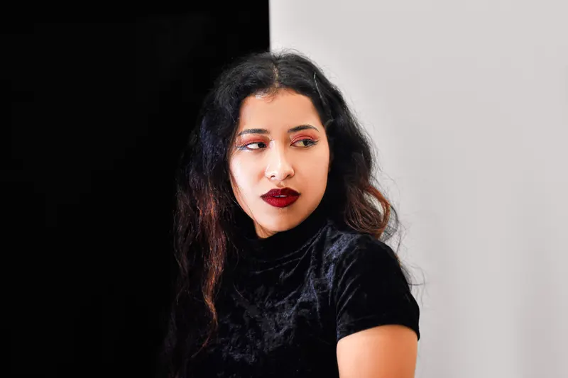 A woman with dark wavy hair wears a deep velvet top and a wine colored lip.