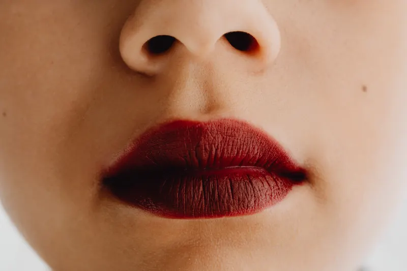A close-up of lips in a deep black cherry lipstick.