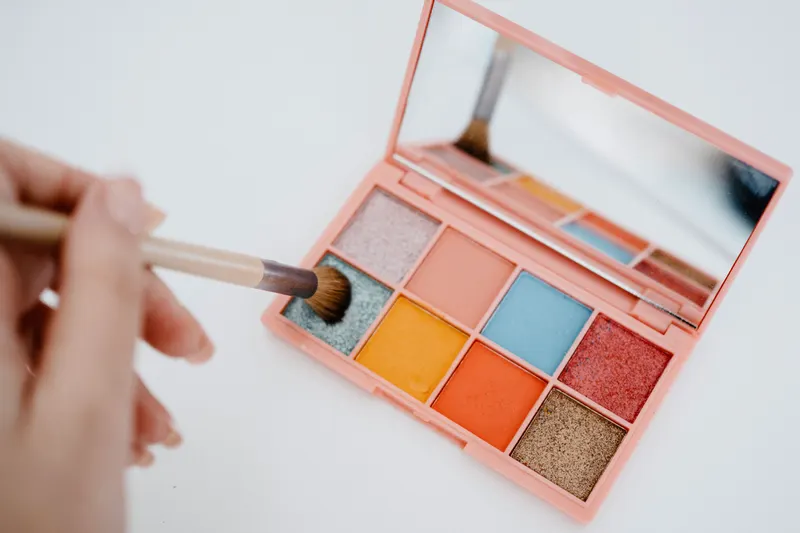 Brush dipping into an eyeshadow palette with orange, blue, pink and gold shades