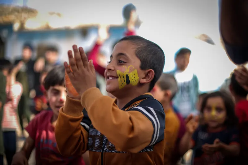 Smiling boy clapping at a party with a small yellow butterfly painted on his cheek