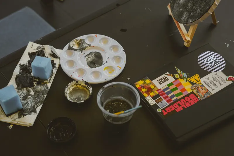 Face painting setup with sponges, a paint palette, brushes and a cup of water on a table