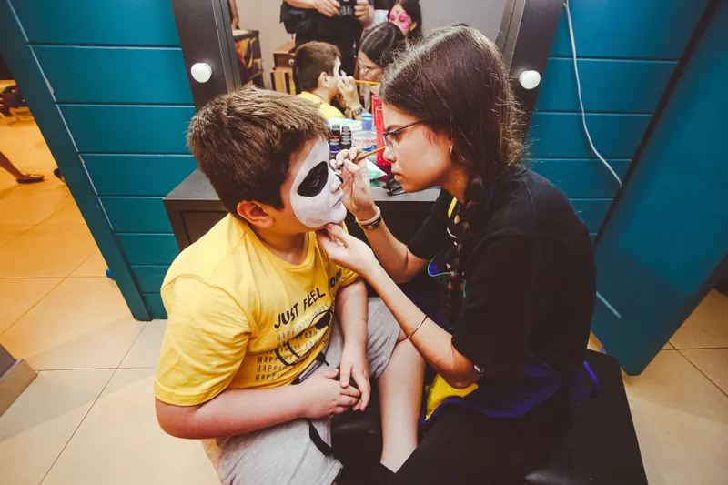 A young face painter carefully paints a boy's face at an indoor party
