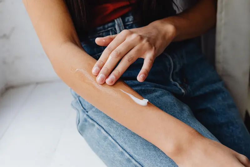 A fingertip spreads a small dab of cream on the inner forearm