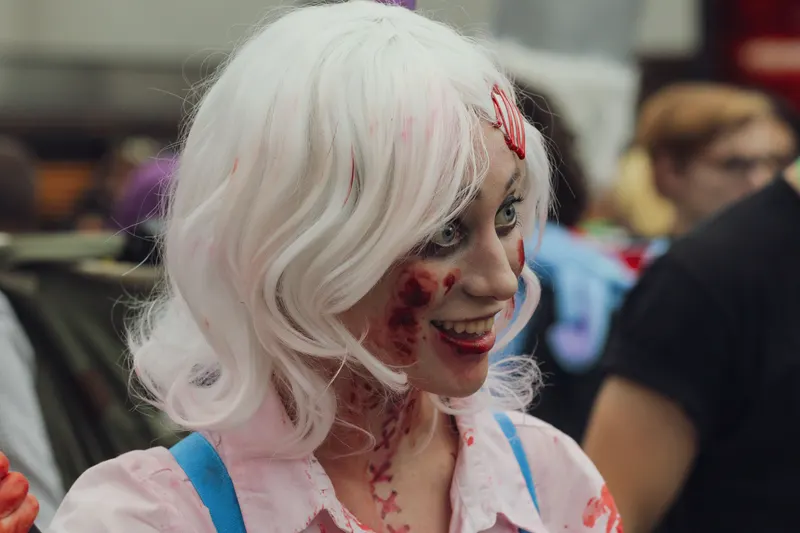 Smiling person in a white wig with fake blood and scratch effects painted on the cheek
