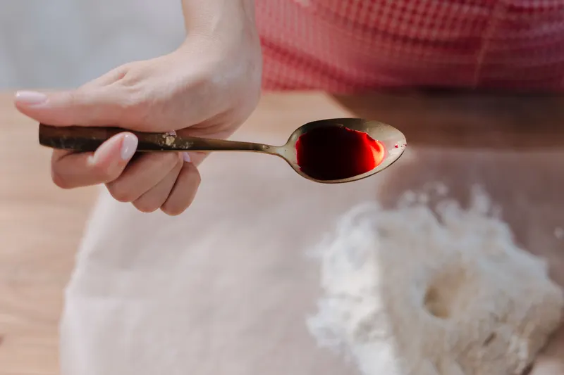 A spoonful of red syrup held over a bowl of flour