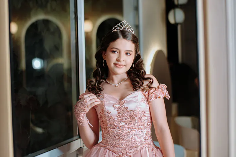 Quinceanera in a pink gown with her hair styled down in curls under a tiara
