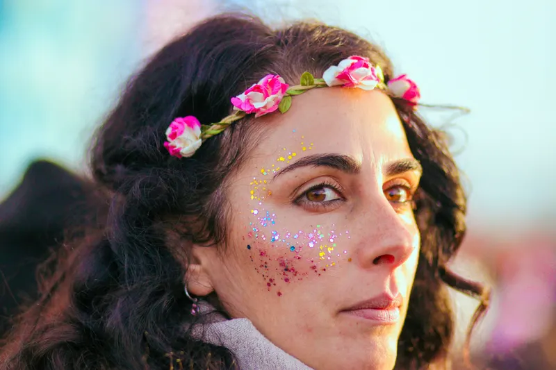 Woman in a flower crown with pink and gold glitter on her cheek, kept away from her eyes