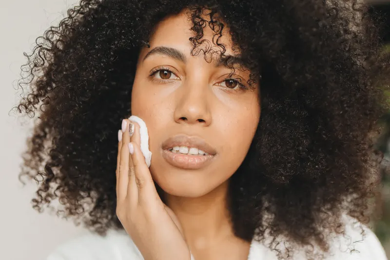 Woman with curly hair wiping her cheek with a cotton pad