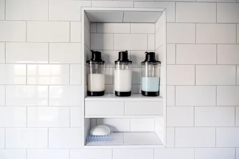 Three unlabelled pump bottles of hair care in a tiled shower niche