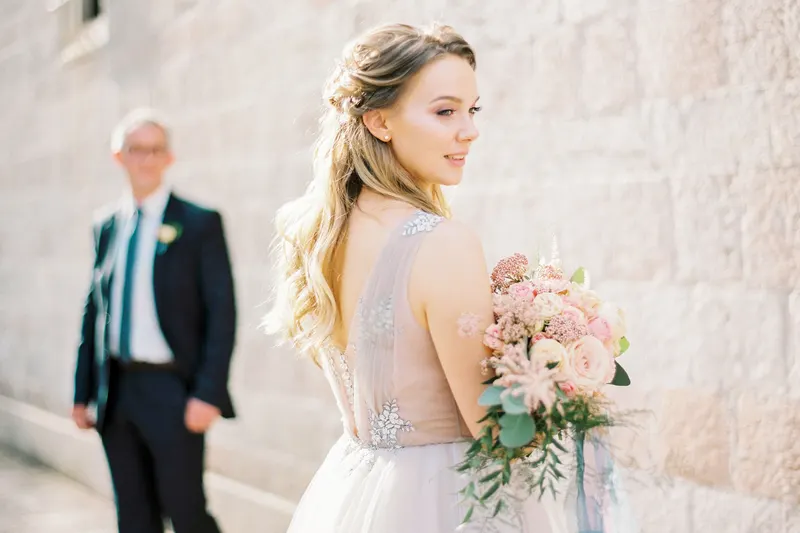 A bride with long, loose half-up waves walks beside her father