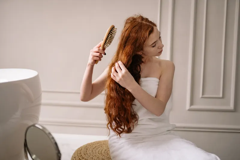 A woman in a towel brushes her long red hair after washing