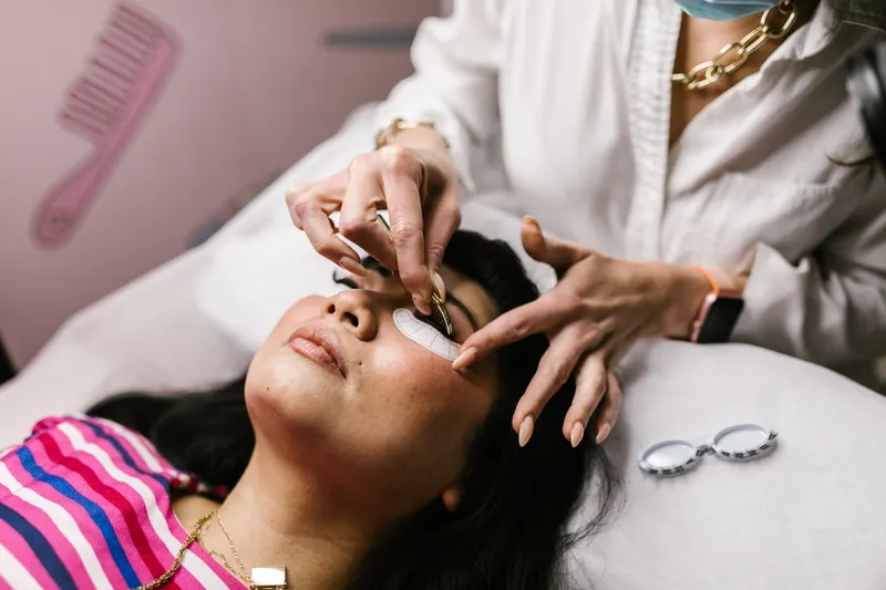 A lash artist works on a client lying back with under-eye pads in a salon, the kind of appointment that sets how long lash extensions last.