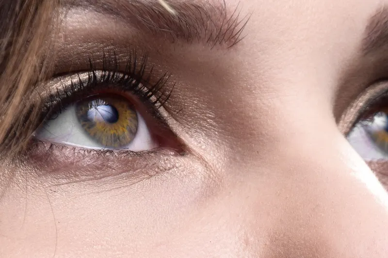 A close-up of hazel eyes looking upward with dark, lifted and curled lashes, the look people weigh in lash lift vs lash extensions.