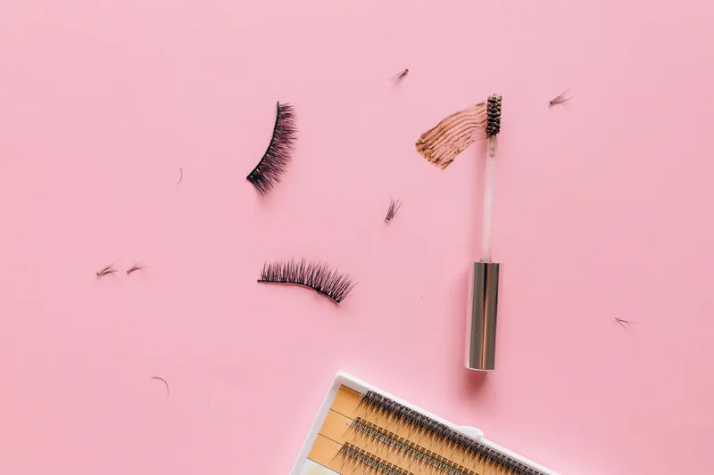 Strip lashes, a lash spoolie and a tray of individual lashes laid out on a pink surface, the pieces a lash map helps arrange.