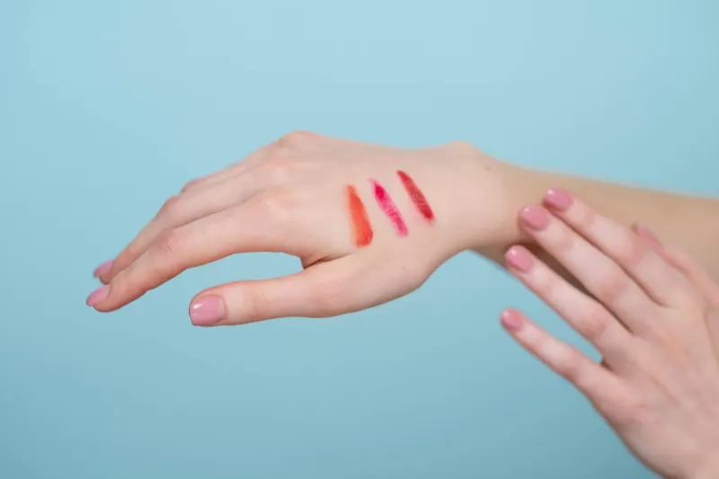 Swatches of coral, pink and red lipstick on the back of a hand