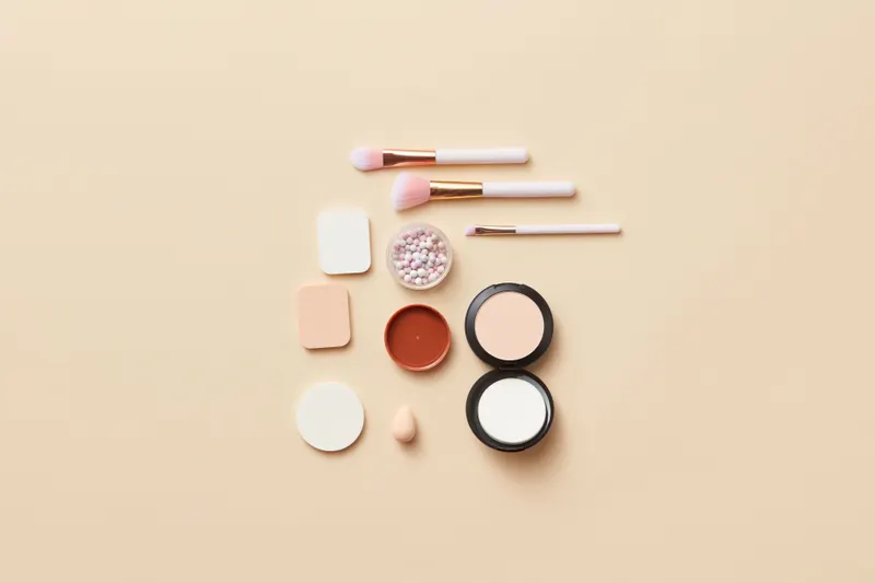 Makeup sponges, brushes, a powder compact and cream products laid out in neat rows, ready to use in the order of makeup application.