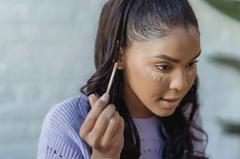 Woman applying concealer in small triangles under her eyes with a brush