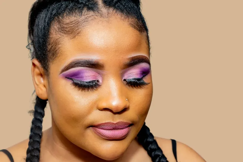 A woman with braids wears blended violet and purple eyeshadow and a soft pink lip