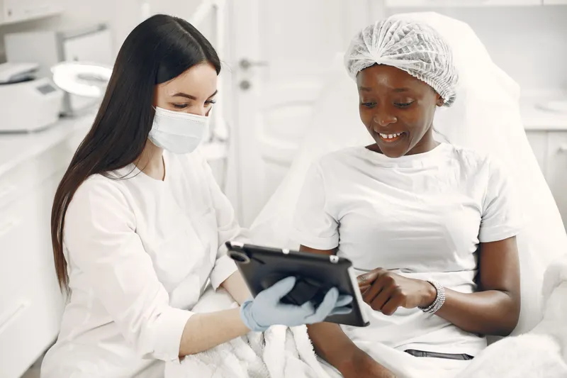 A dermatologist with a tablet talks a smiling patient through her skin