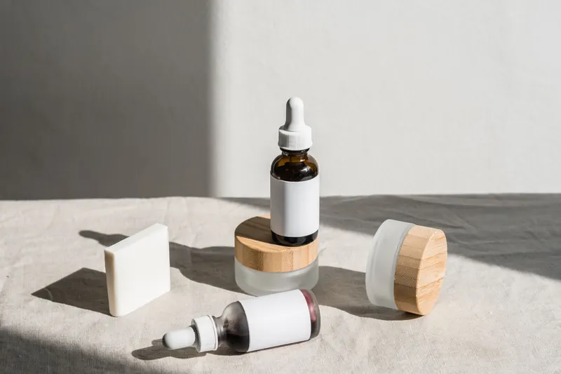 Unbranded skincare bottles and jars with blank labels on a linen cloth