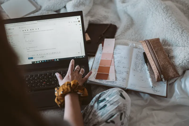 A woman writes an email on a laptop beside a planner and color swatches