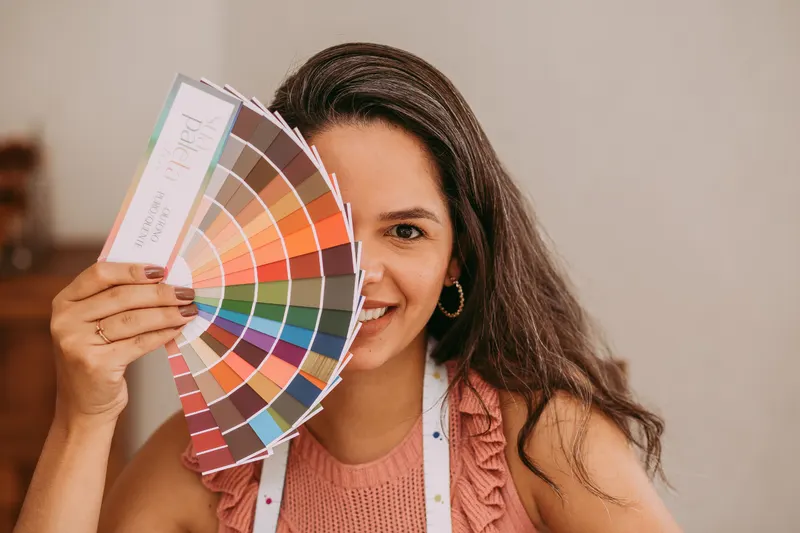 A smiling woman holds a fan of color swatches beside her face, the kind of comparison a seasonal color analysis quiz helps with.