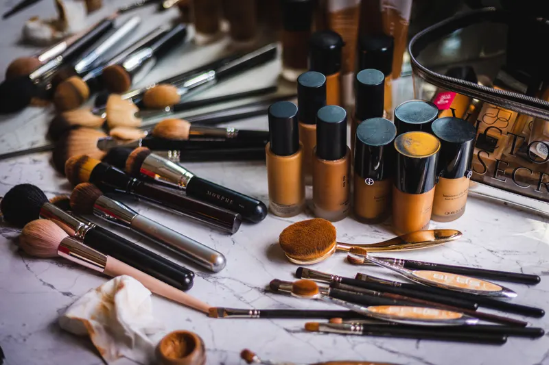 Rows of foundation bottles in light to deep shades lined up with makeup brushes and sponges.