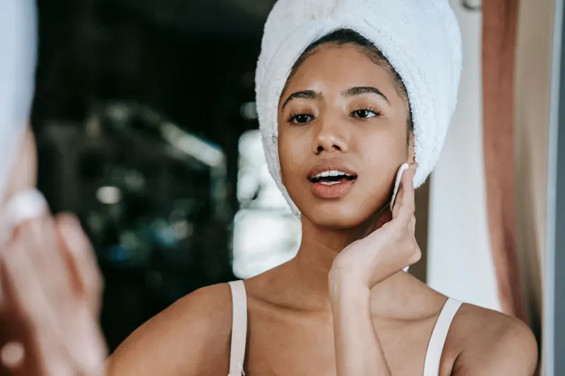 Woman in a hair towel smoothing moisturizer onto her cheek