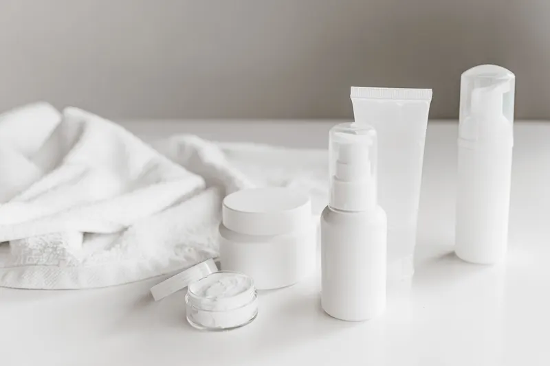 Unlabeled skincare bottles, a pump, a tube and a cream jar on a white towel