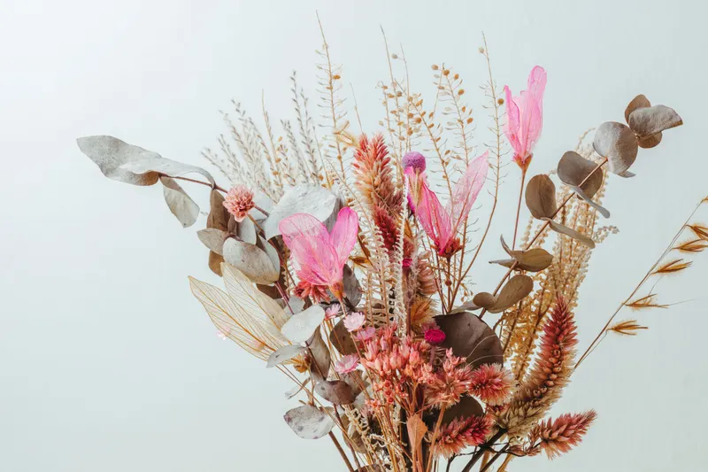 A dried flower bouquet of sage leaves, wheat and dusty pink blooms, the soft earth tones of a soft autumn color palette.