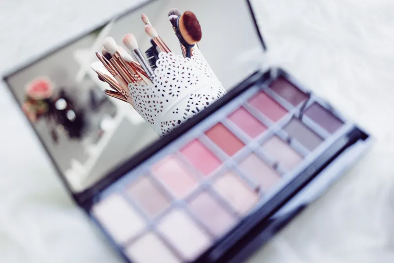 An open eyeshadow palette in soft lilac, mauve and gray-pink shades next to makeup brushes.