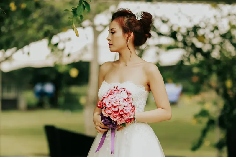 Bride in a strapless wedding gown with her hair in an updo, holding pink roses outdoors