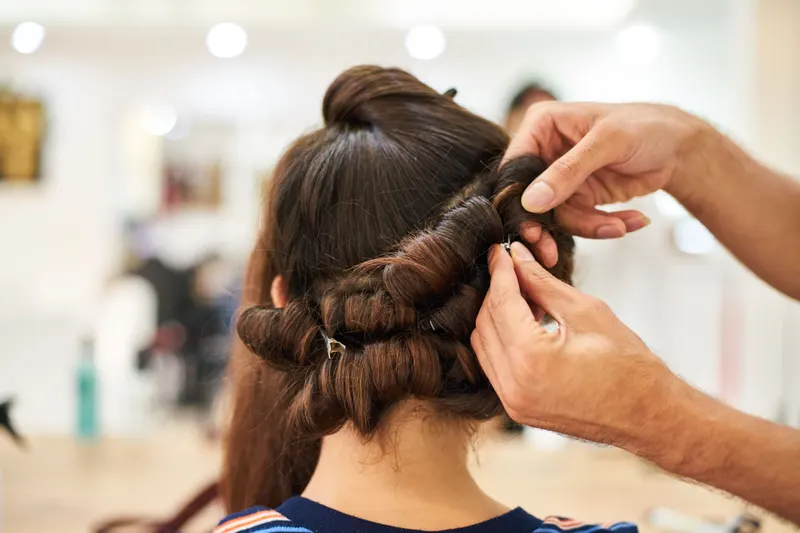 Hairstylist pinning rolled sections of dark hair into place for an updo