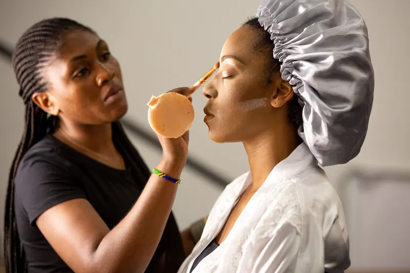 A makeup artist presses foundation onto a client's cheek with a sponge, the in-person shade check that confirms what an undertone finder suggests.