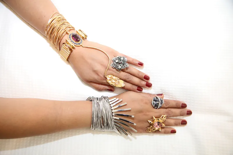 Two hands on a white background, one stacked with gold bracelets and rings and the other with silver bangles, the side-by-side comparison the undertone finder's jewelry check uses.
