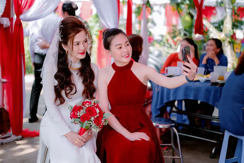 Wedding guest in a red halter dress with long waves, taking a selfie with the bride