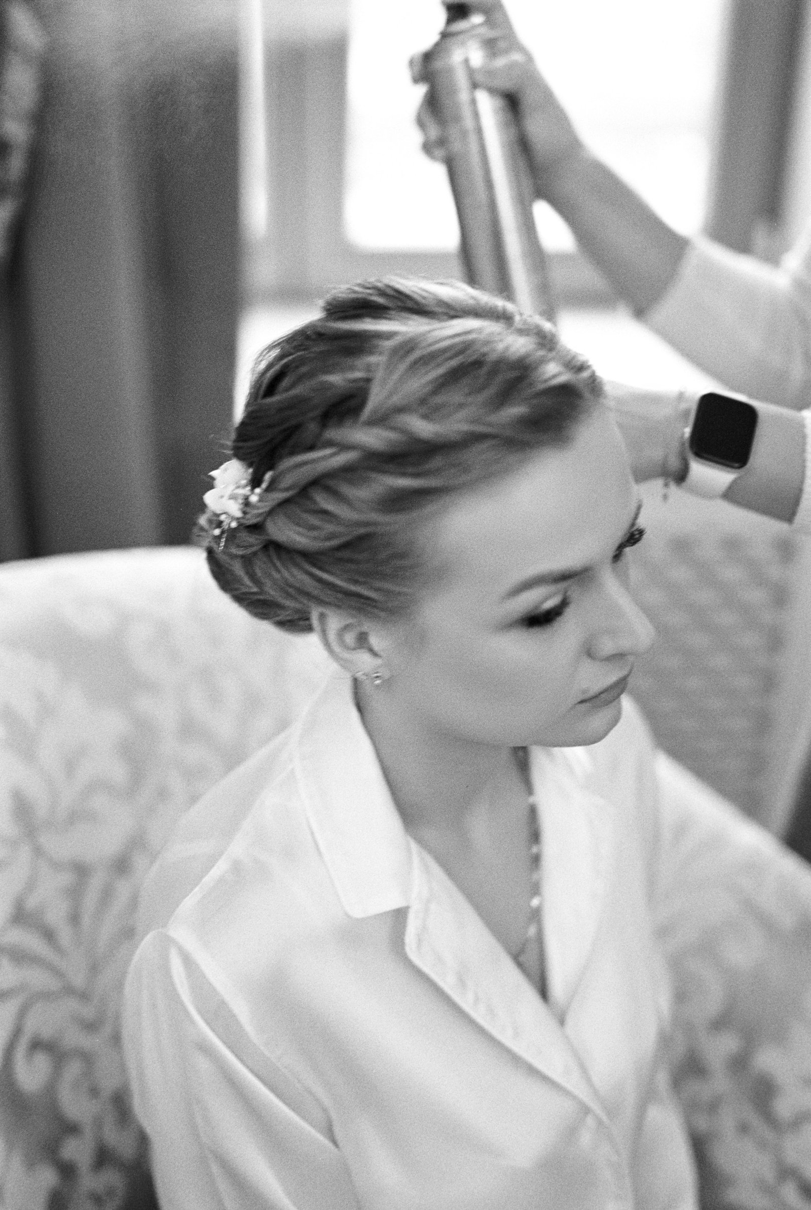 A woman having an elegant wedding guest hairstyle finished with soft braided texture before a formal event.