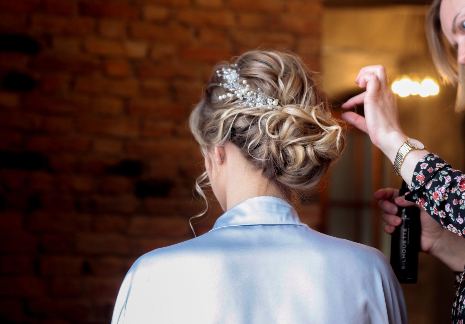 A wedding hair stylist finishes styling soft curls into an updo for a bride getting ready on her wedding day.