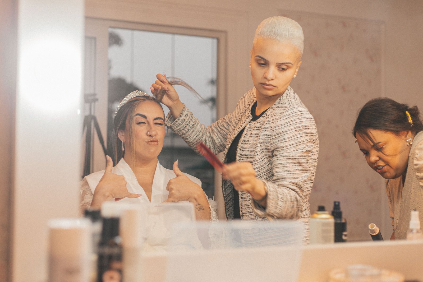 Two professional stylists work together on a bride, giving final touches as a combined hair and makeup artist team.
