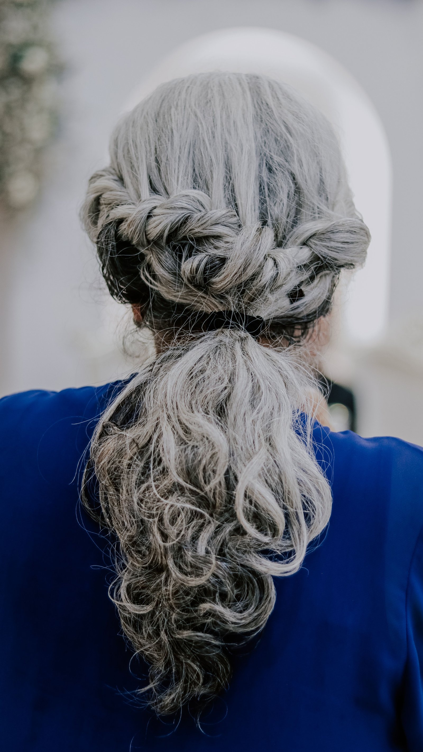 An elegant mother of the bride hairstyle featuring natural gray hair in a soft braided half-up style.